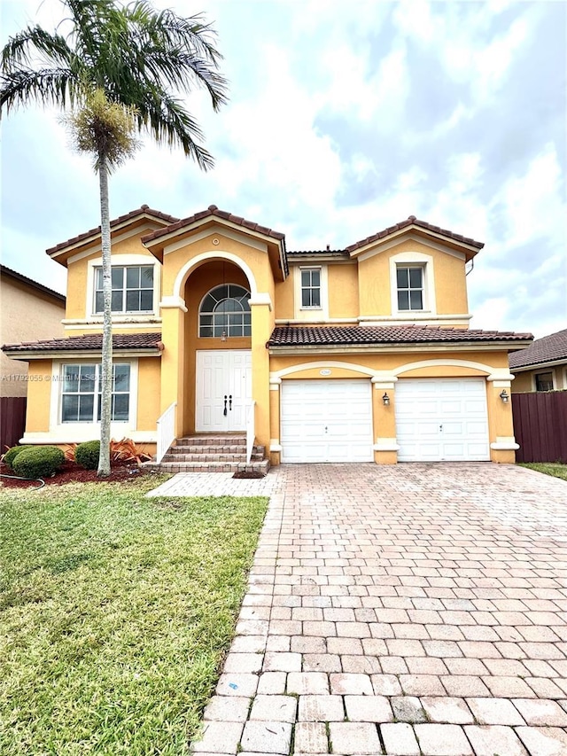 mediterranean / spanish home featuring a front yard, decorative driveway, fence, an attached garage, and stucco siding