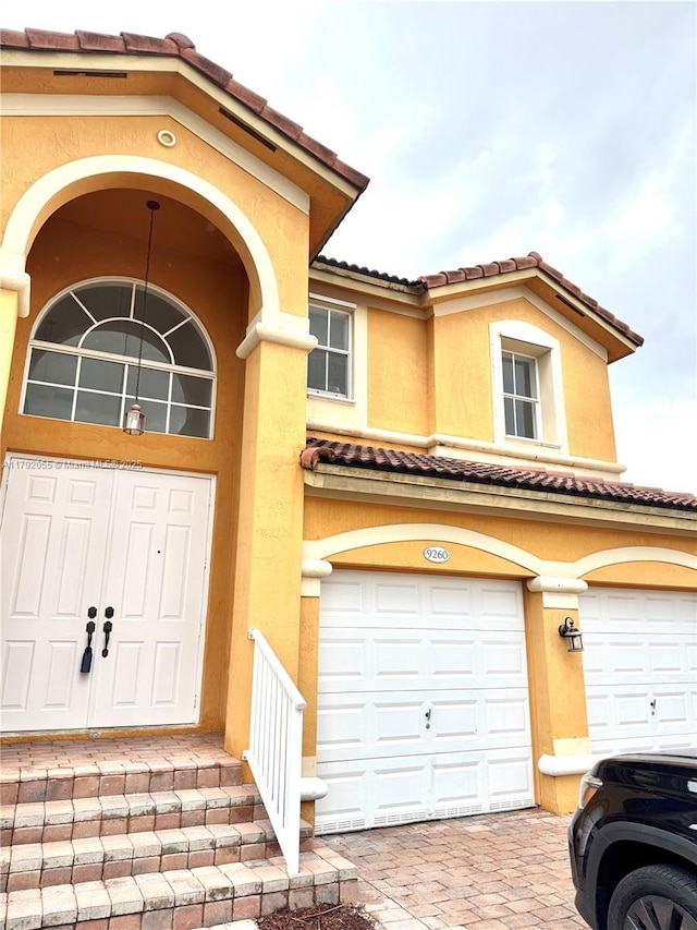view of exterior entry featuring a tiled roof, decorative driveway, a garage, and stucco siding
