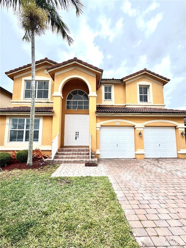 mediterranean / spanish house with an attached garage, decorative driveway, a front lawn, and stucco siding