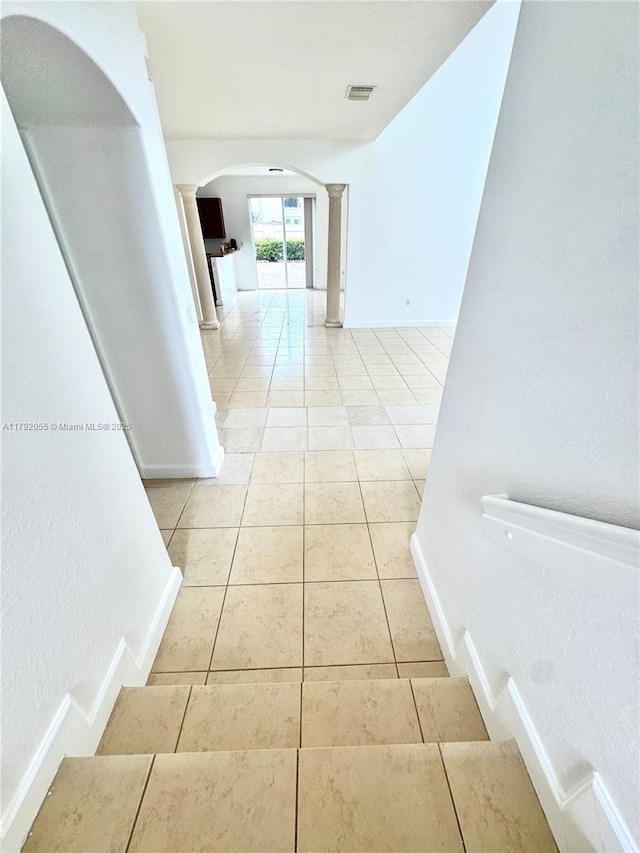 stairway featuring arched walkways, decorative columns, tile patterned flooring, and visible vents