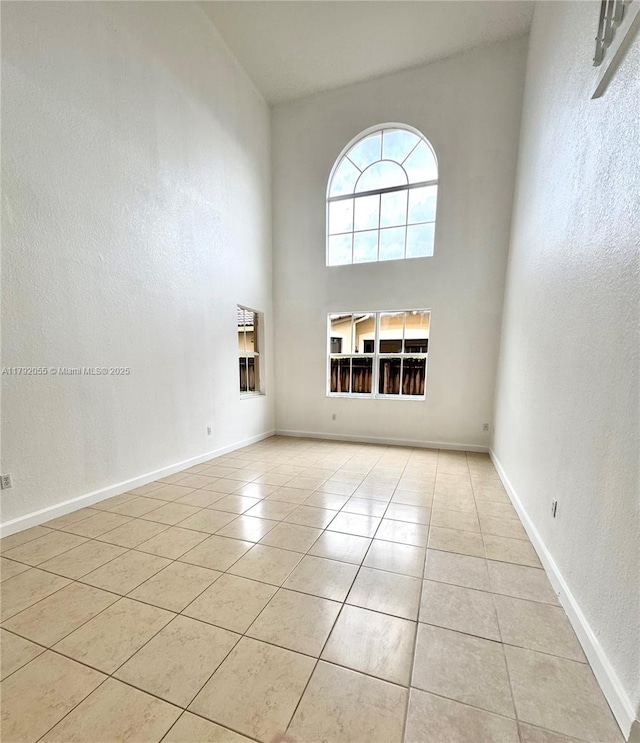 empty room with baseboards, a textured wall, light tile patterned flooring, and a towering ceiling