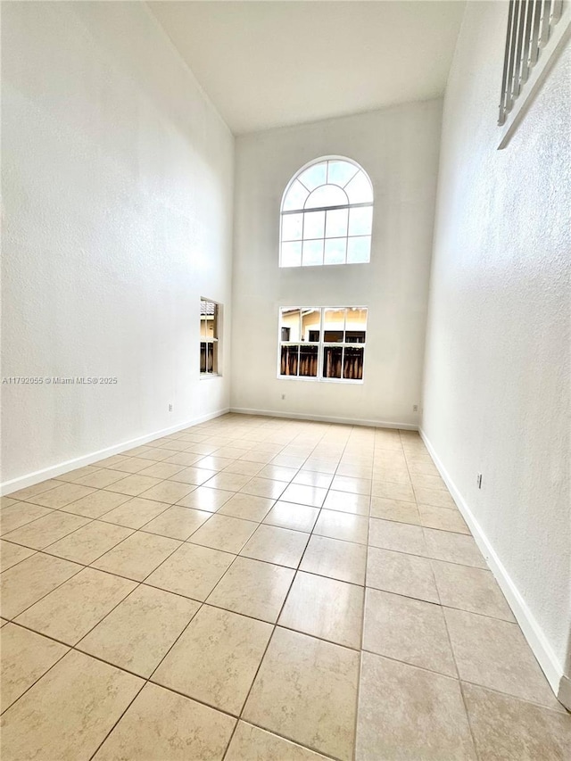 unfurnished room featuring baseboards, tile patterned flooring, and a high ceiling