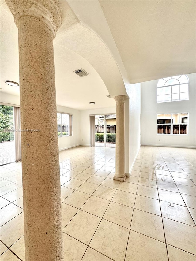 empty room with arched walkways, baseboards, decorative columns, light tile patterned floors, and visible vents