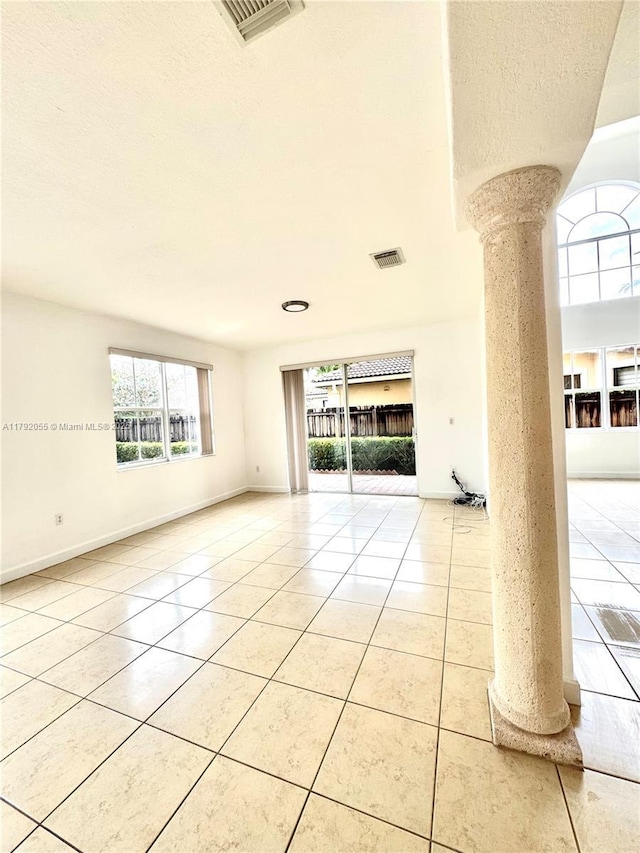 unfurnished room with ornate columns, light tile patterned flooring, and a wealth of natural light