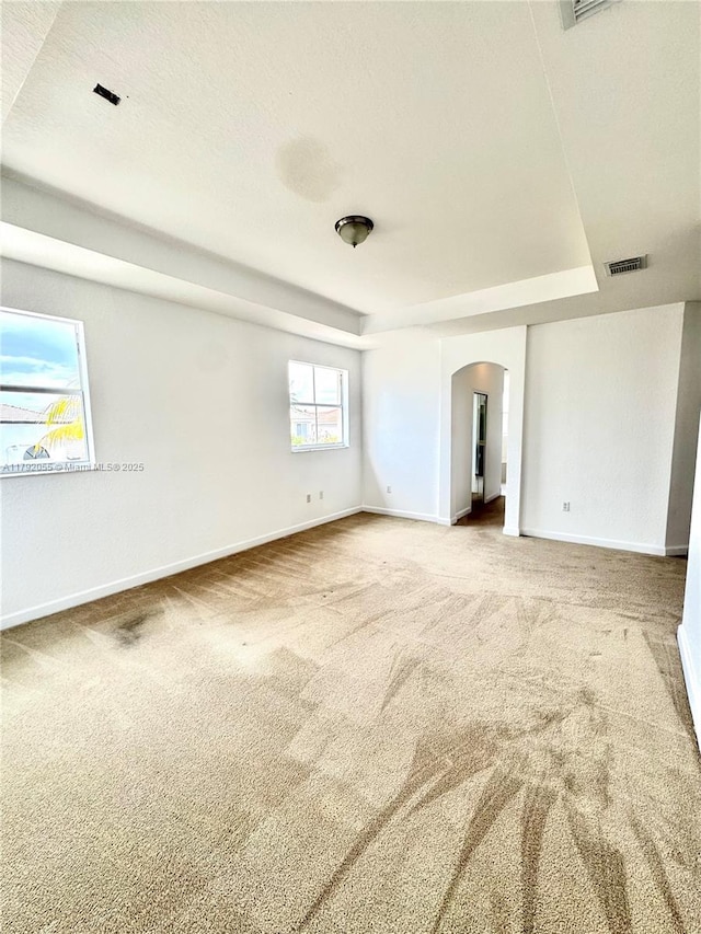 carpeted empty room featuring arched walkways, baseboards, visible vents, and a raised ceiling