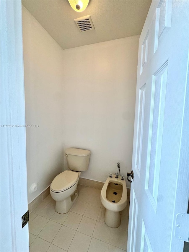 bathroom with tile patterned flooring, toilet, baseboards, visible vents, and a bidet