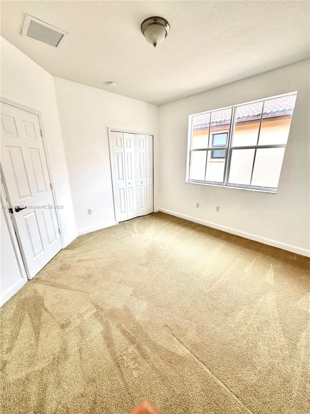 unfurnished bedroom with a textured ceiling, visible vents, baseboards, a closet, and carpet flooring