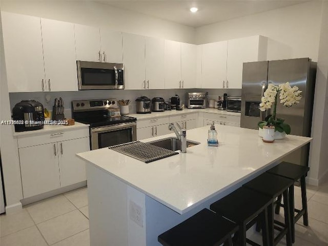 kitchen with light tile patterned flooring, a breakfast bar area, light countertops, stainless steel appliances, and white cabinetry