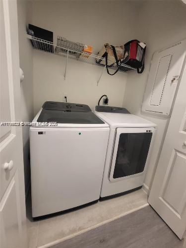 washroom featuring electric panel, laundry area, light wood finished floors, and washing machine and clothes dryer