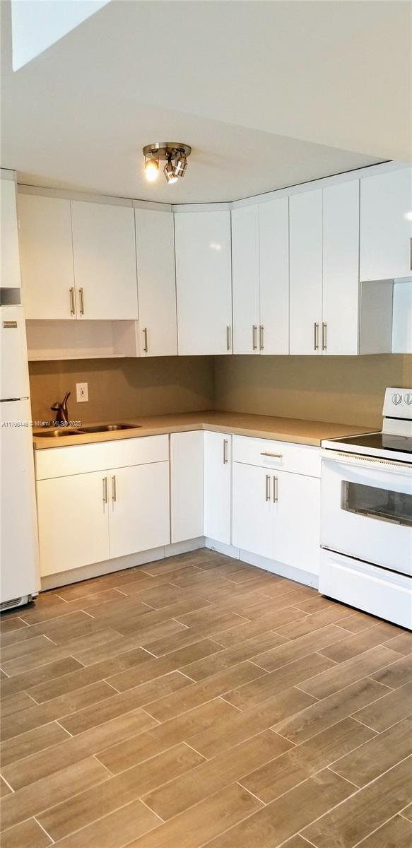 15205 NE 6th Ave Unit D204, Miami, FL 33162 - kitchen with white cabinetry, white appliances, light wood-type flooring, and a sink