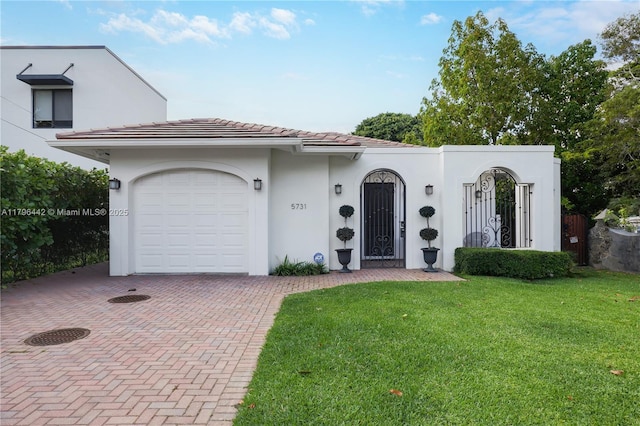 mediterranean / spanish home with an attached garage, a tiled roof, stucco siding, a front lawn, and decorative driveway