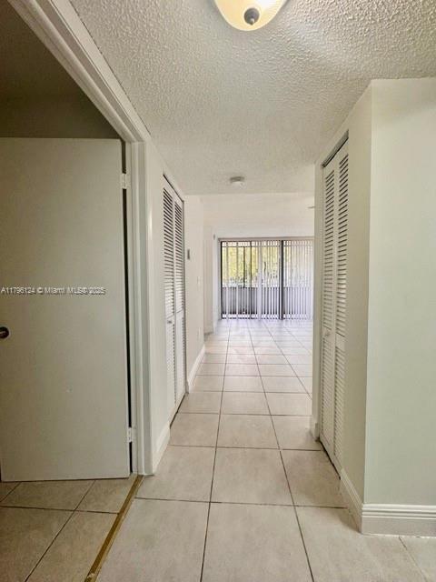 hallway with baseboards, light tile patterned flooring, and a textured ceiling