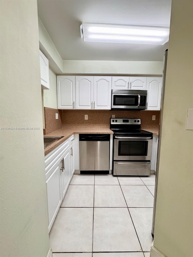 kitchen with a sink, light tile patterned flooring, white cabinetry, and appliances with stainless steel finishes