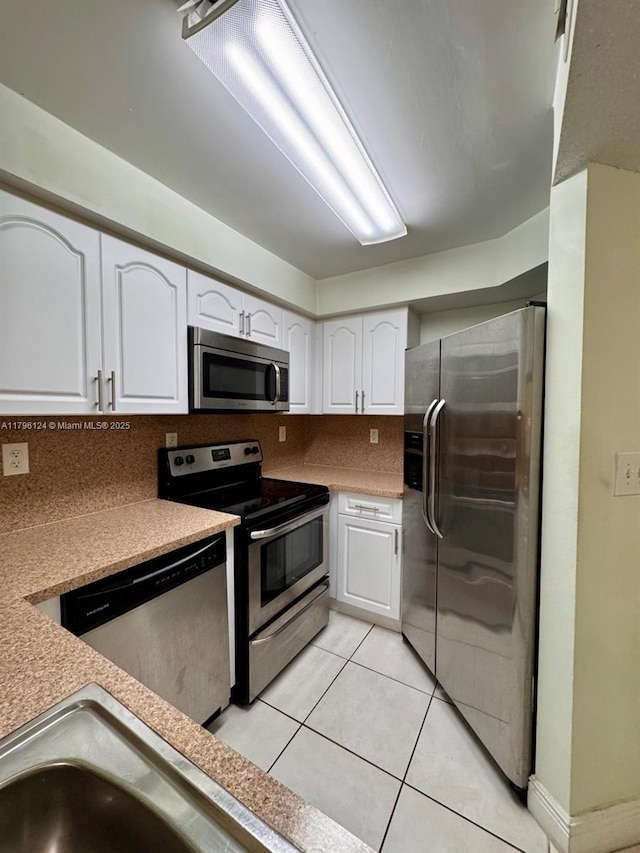 kitchen with stainless steel appliances, tasteful backsplash, light countertops, light tile patterned floors, and white cabinets