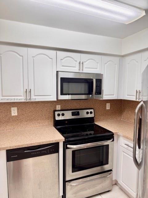 kitchen featuring stainless steel appliances, white cabinetry, decorative backsplash, and light countertops