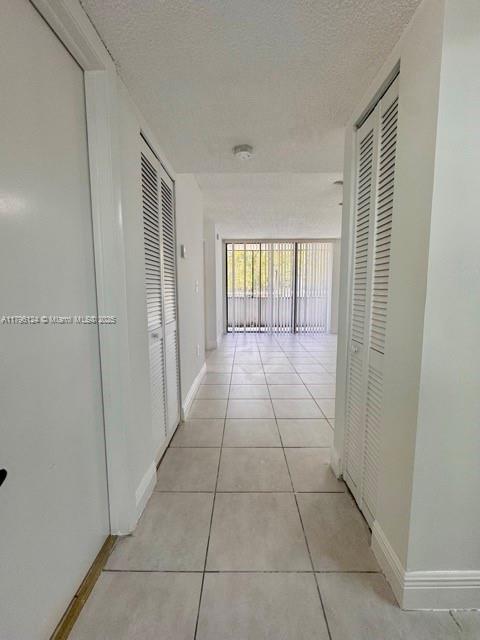hall featuring a textured ceiling, baseboards, and light tile patterned floors