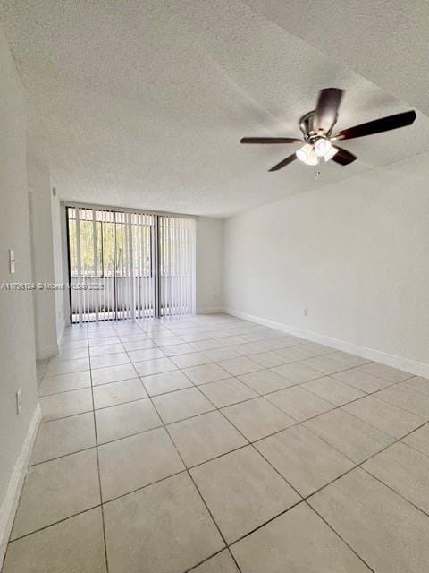 spare room featuring a textured ceiling, baseboards, a ceiling fan, and light tile patterned floors