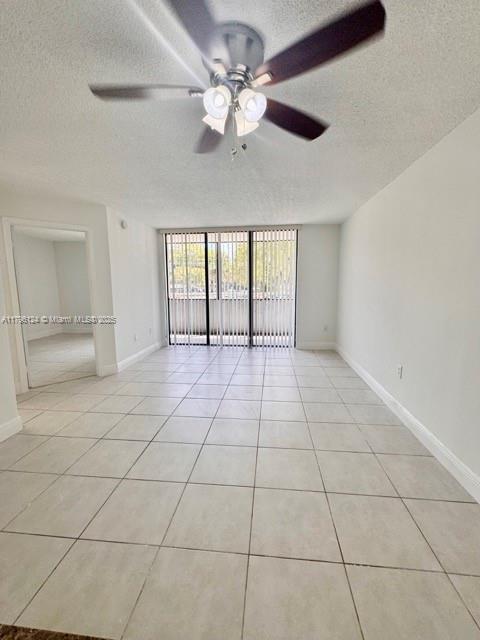 unfurnished room with ceiling fan, a textured ceiling, baseboards, and light tile patterned floors