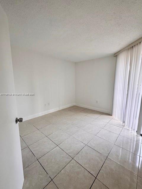 spare room featuring light tile patterned floors, baseboards, and a textured ceiling