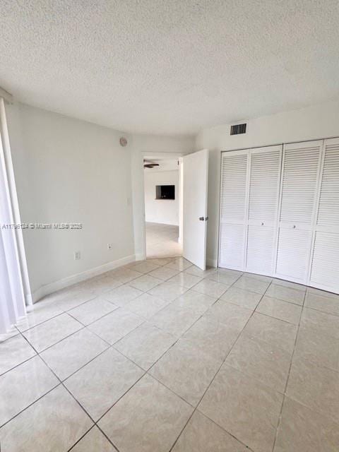 unfurnished bedroom with a textured ceiling, a closet, light tile patterned floors, and visible vents