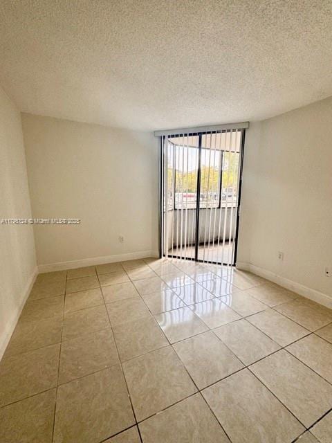 spare room with light tile patterned floors, baseboards, and a textured ceiling