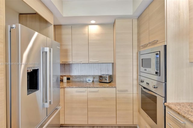 kitchen with light stone countertops, light brown cabinetry, modern cabinets, and appliances with stainless steel finishes