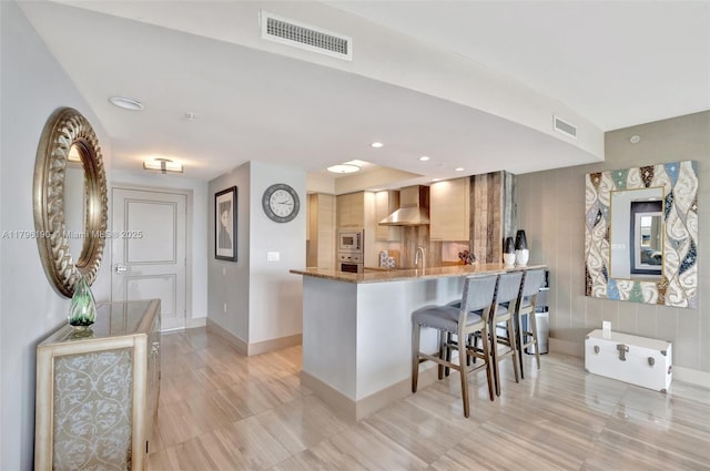 kitchen with stainless steel appliances, wall chimney range hood, a kitchen bar, and visible vents