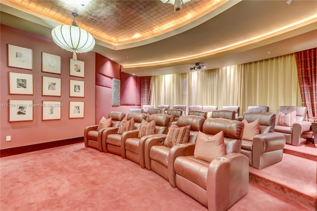 carpeted home theater featuring a tray ceiling and baseboards