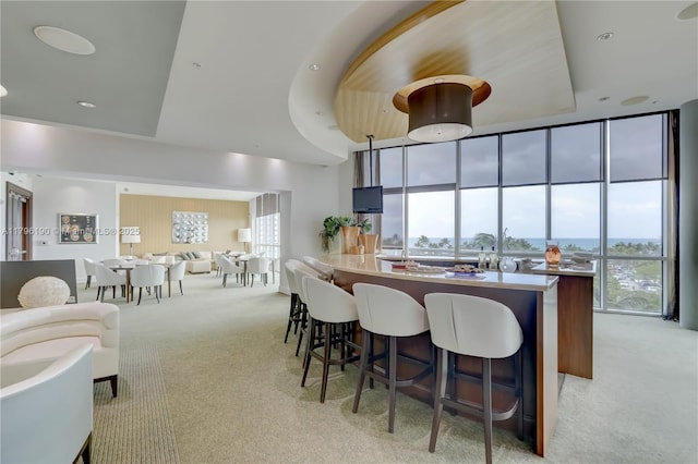 kitchen with a breakfast bar, a wall of windows, a peninsula, a towering ceiling, and light carpet