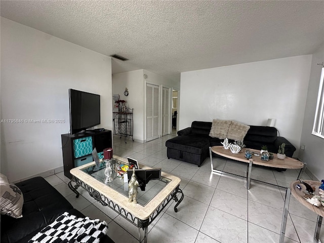living area with baseboards, light tile patterned floors, visible vents, and a textured ceiling