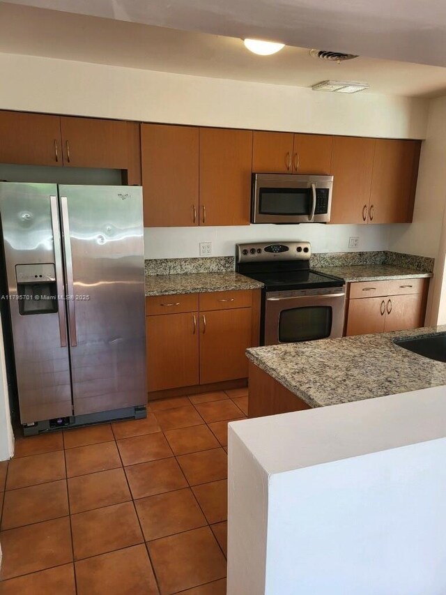 kitchen with light tile patterned floors, brown cabinets, a sink, stainless steel appliances, and visible vents