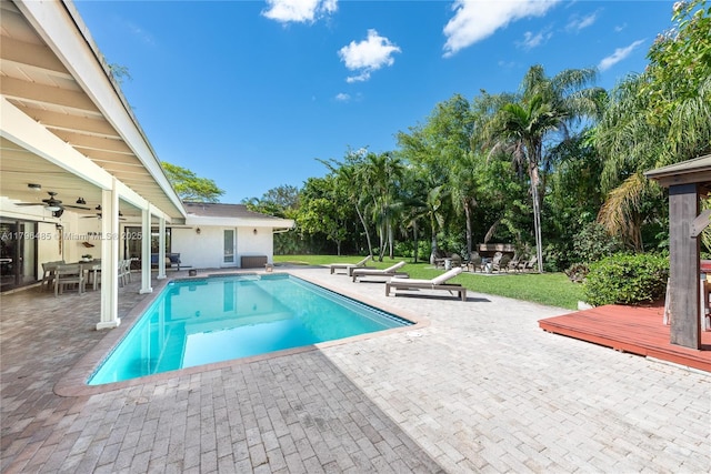 pool with ceiling fan, a patio area, outdoor dining area, and a lawn