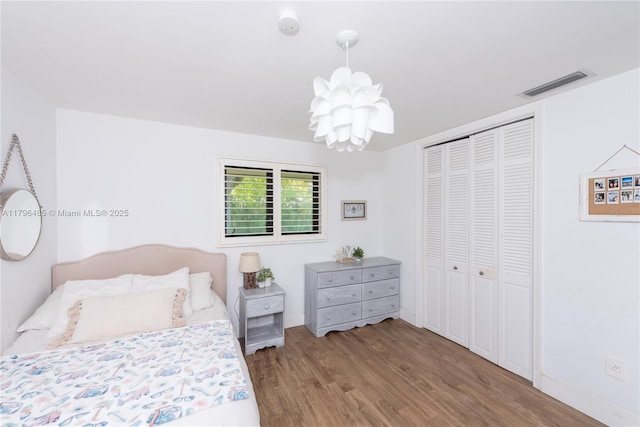 bedroom featuring a closet, wood finished floors, visible vents, a notable chandelier, and baseboards