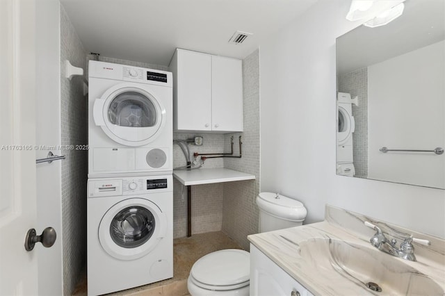 bathroom with stacked washer / dryer, vanity, toilet, and visible vents