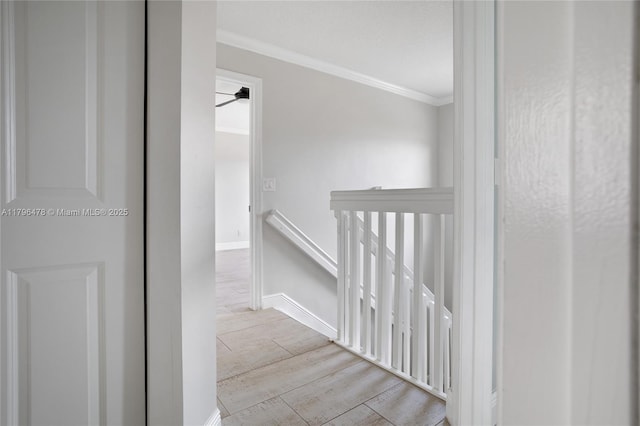 corridor featuring baseboards, ornamental molding, an upstairs landing, and wood finished floors