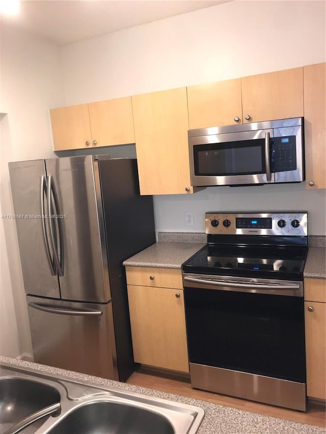 kitchen with a sink, light brown cabinetry, light countertops, and appliances with stainless steel finishes
