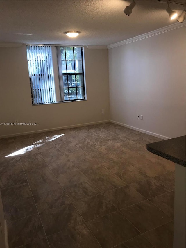 empty room with baseboards, ornamental molding, dark tile patterned flooring, and a textured ceiling
