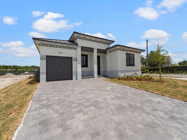 prairie-style house with a standing seam roof, decorative driveway, an attached garage, stucco siding, and a front lawn
