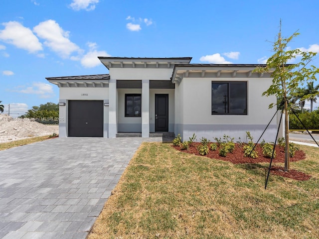 prairie-style house featuring a standing seam roof, decorative driveway, a garage, stucco siding, and a front lawn