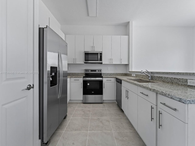 kitchen with light tile patterned floors, a sink, stainless steel appliances, white cabinets, and light stone countertops