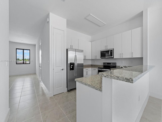 kitchen with a peninsula, white cabinets, stainless steel appliances, and light stone countertops