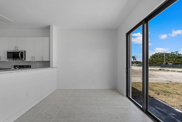 kitchen featuring stainless steel microwave, light countertops, light tile patterned floors, and white cabinets