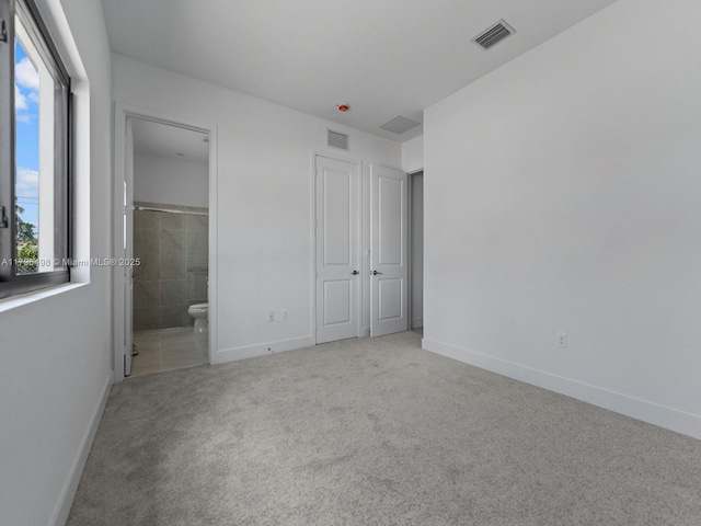 unfurnished bedroom featuring ensuite bath, visible vents, baseboards, and carpet floors