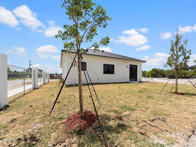 back of house featuring fence, stucco siding, metal roof, a lawn, and a standing seam roof