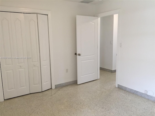 unfurnished bedroom with baseboards, a closet, and speckled floor
