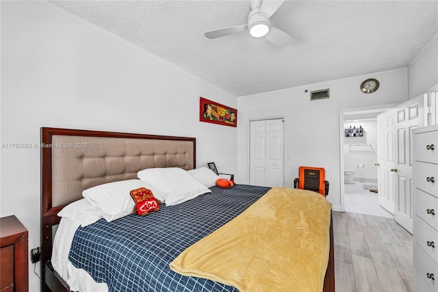 bedroom with a closet, a textured ceiling, ensuite bath, visible vents, and light wood finished floors