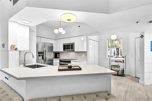 kitchen featuring light wood-style flooring, stainless steel appliances, a sink, a peninsula, and light countertops