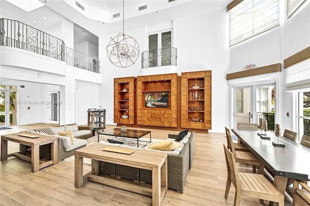 living room featuring a towering ceiling, a notable chandelier, visible vents, and light wood-style floors