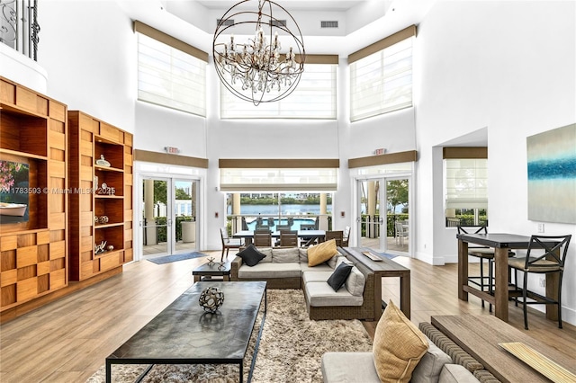 living area with french doors, wood finished floors, a towering ceiling, visible vents, and a notable chandelier