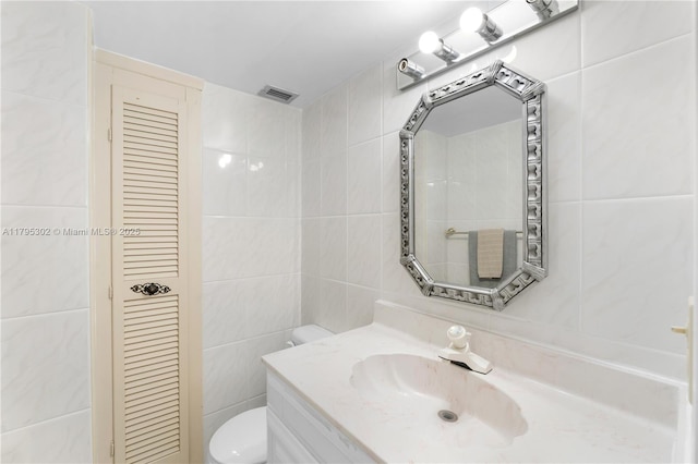 bathroom with toilet, tile walls, vanity, and visible vents